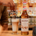 Fles Monin Toasted Marshmellow Siroop met ernaast een latte macchiato met Monin Toasted Marshmellow Siroop als toevoeging.