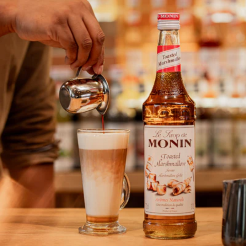 Fles Monin Toasted Marshmellow Siroop met ernaast een latte macchiato met Monin Toasted Marshmellow Siroop als toevoeging.